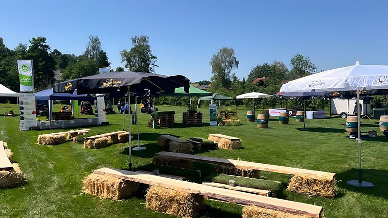 Ausstellungsgelände eines Hoffestes mit Pavillons, Strohballenbänken und bepflanzten Paletten